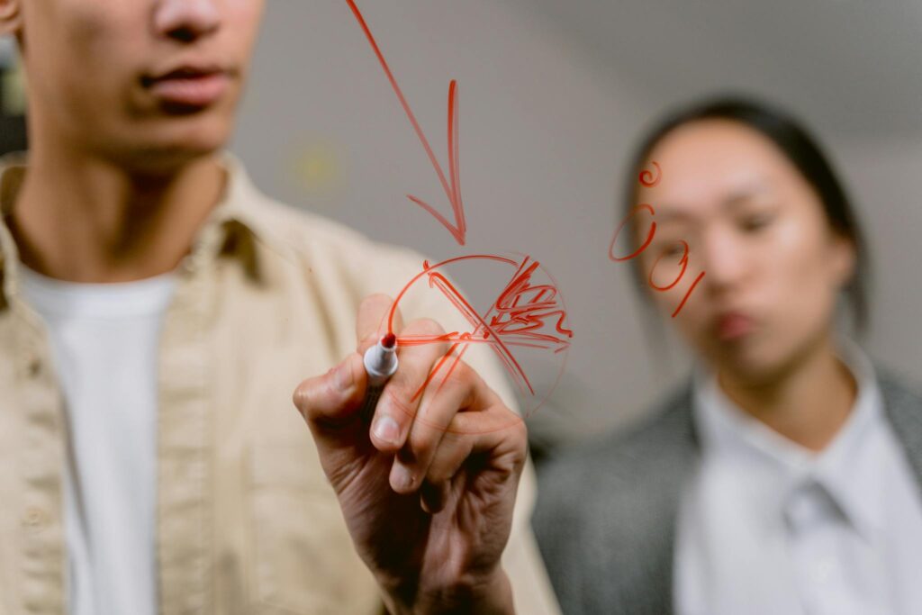 Close-up of hands drawing a concept diagram on glass, symbolizing teamwork and creativity.