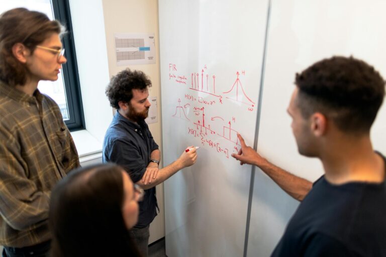 Group of engineers discussing data on a whiteboard during a team meeting.